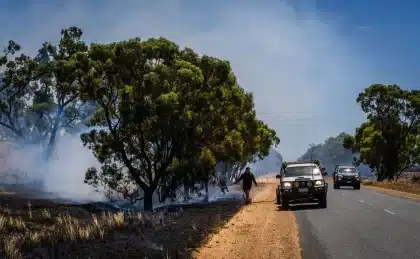 Columna de humo espeso elevándose sobre sierra boscosa con equipos de emergencia en el perímetro