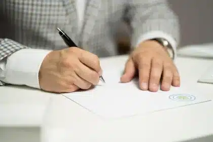 Manos anónimas con sobres y un libro de registro consular sobre una mesa