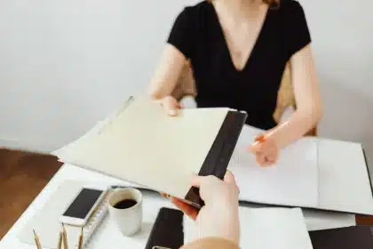 Manos anónimas sobre documentos en una mesa de reunión, con tableta y café