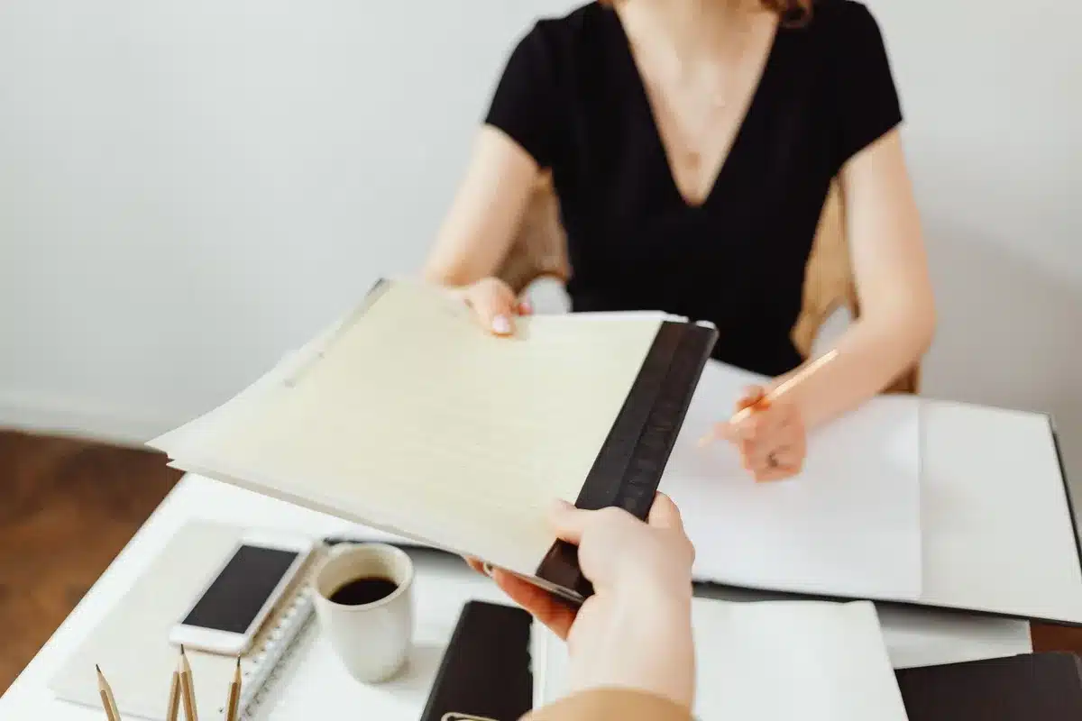 Manos anónimas sobre documentos en una mesa de reunión, con tableta y café